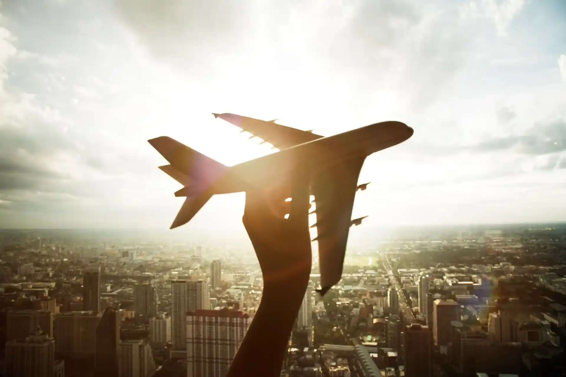 Silhouette d'un avion en vol avec le soleil en arrière-plan, surplombant une ville avec des gratte-ciels et des bâtiments