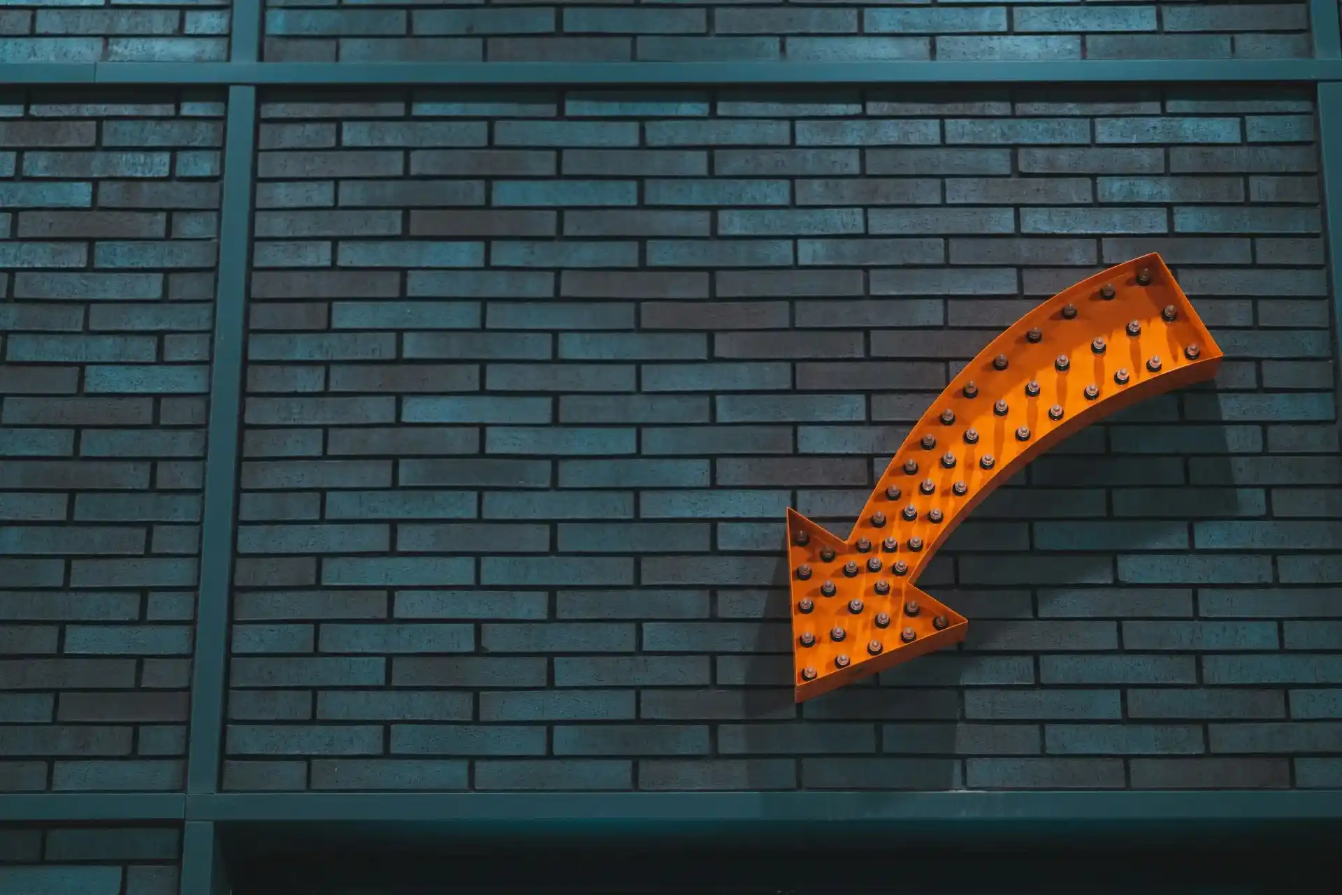 Flèche lumineuse orange pointant vers le bas à droite, fixée sur un mur de briques grises