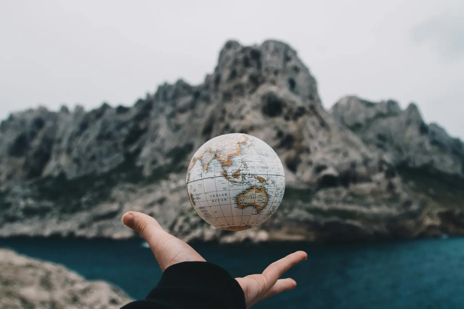 Main tenant un globe terrestre devant des montagnes