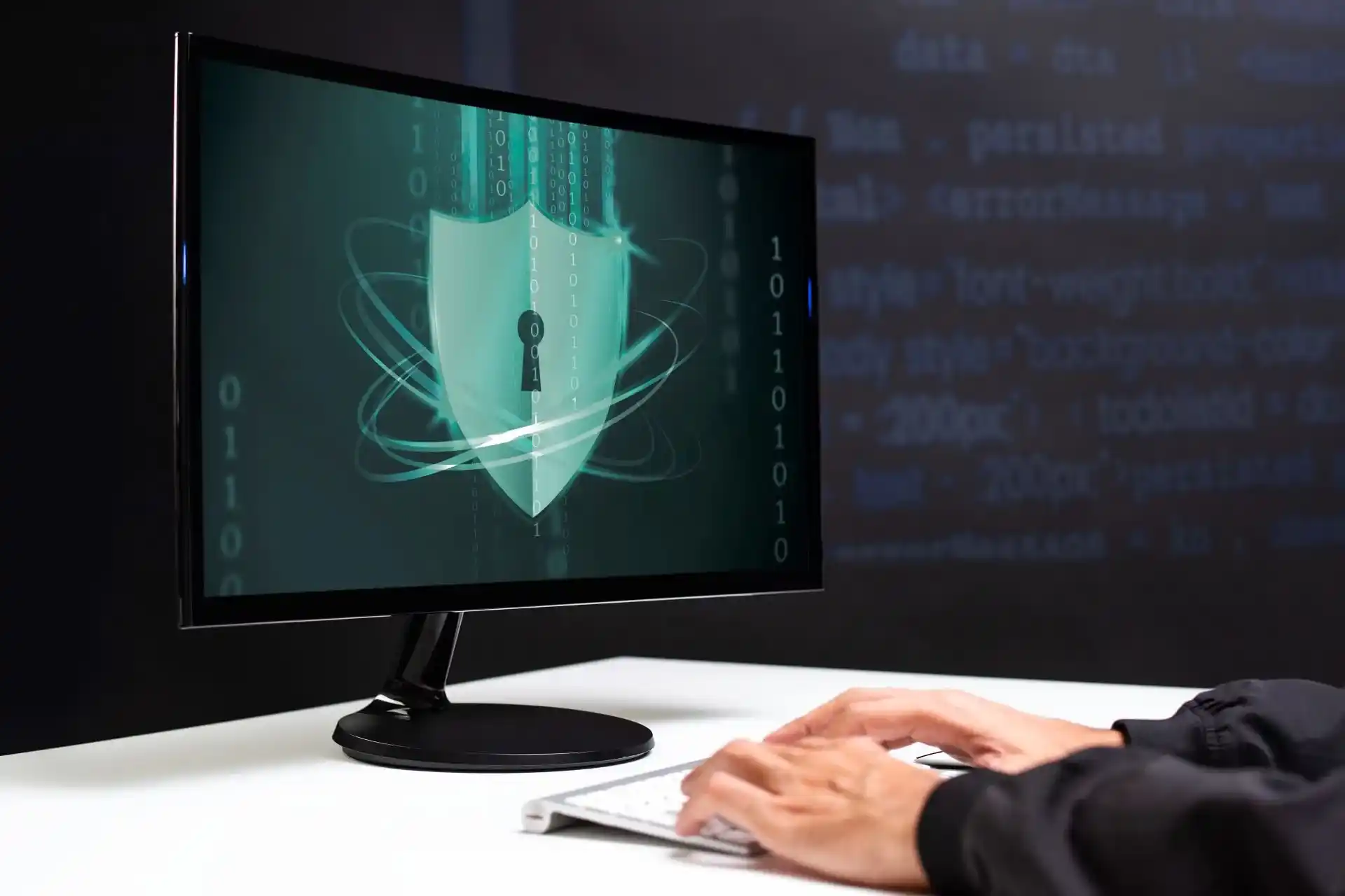 Écran d'ordinateur affichant un bouclier de sécurité avec des codes binaires, une personne utilisant un clavier et une souris